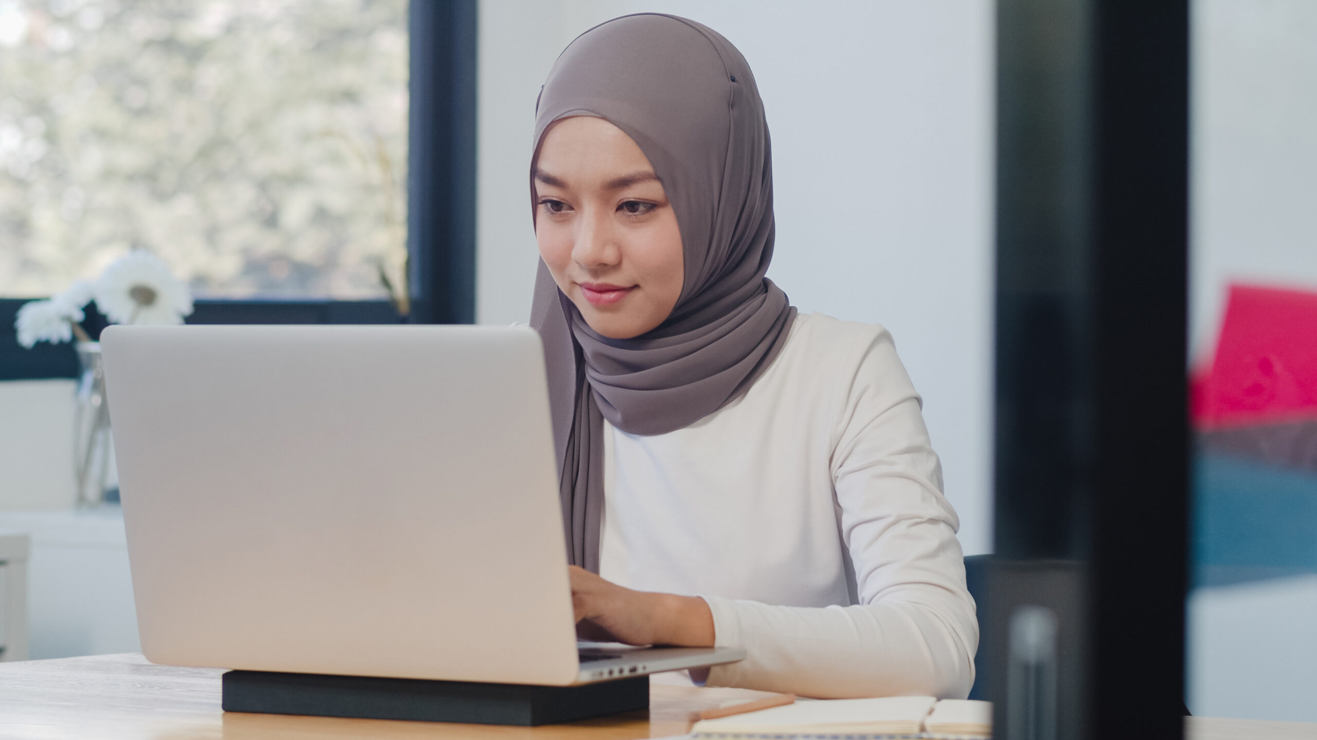 Beautiful Asia muslim lady casual wear working using laptop in modern new normal office. Working from home, remotely work, self isolation, social distancing, quarantine for coronavirus prevention.